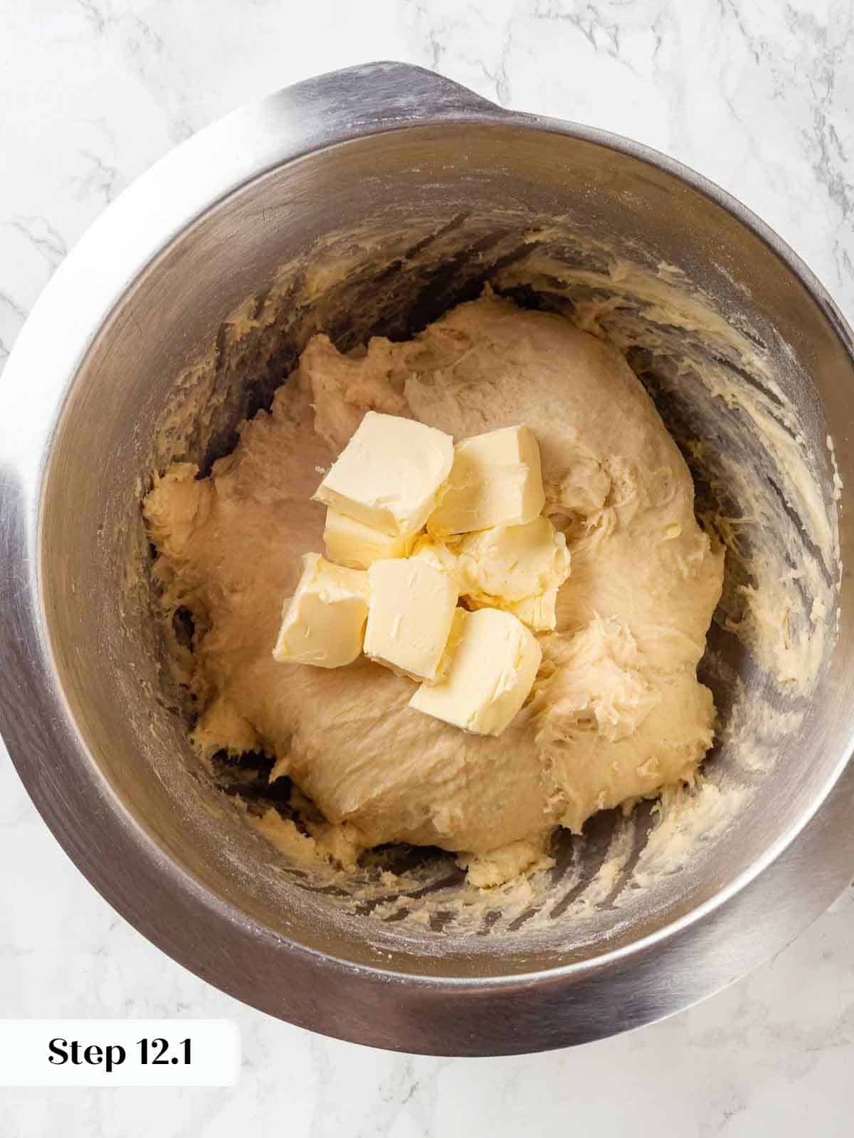 Cubes of butter being added to the mixing bowl with dough in progress.