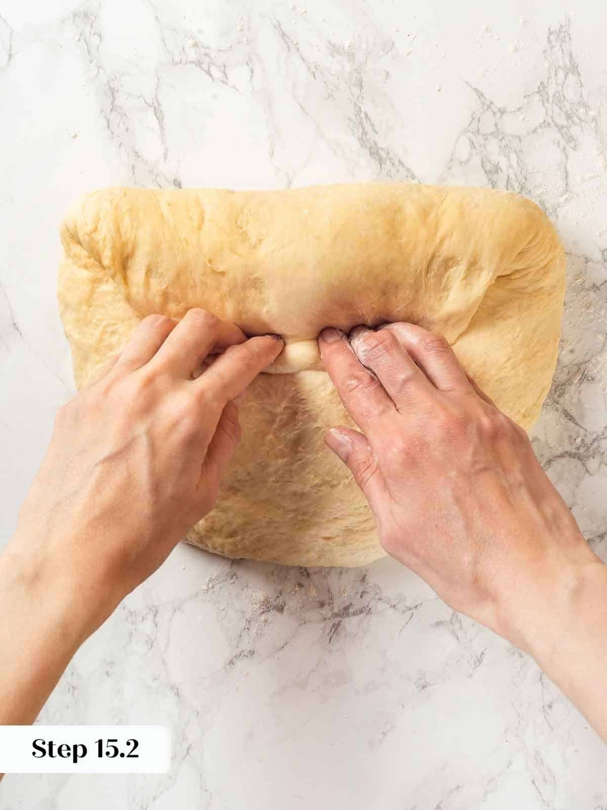 A baker carefully folding potato bread dough into a compact shape for shaping.