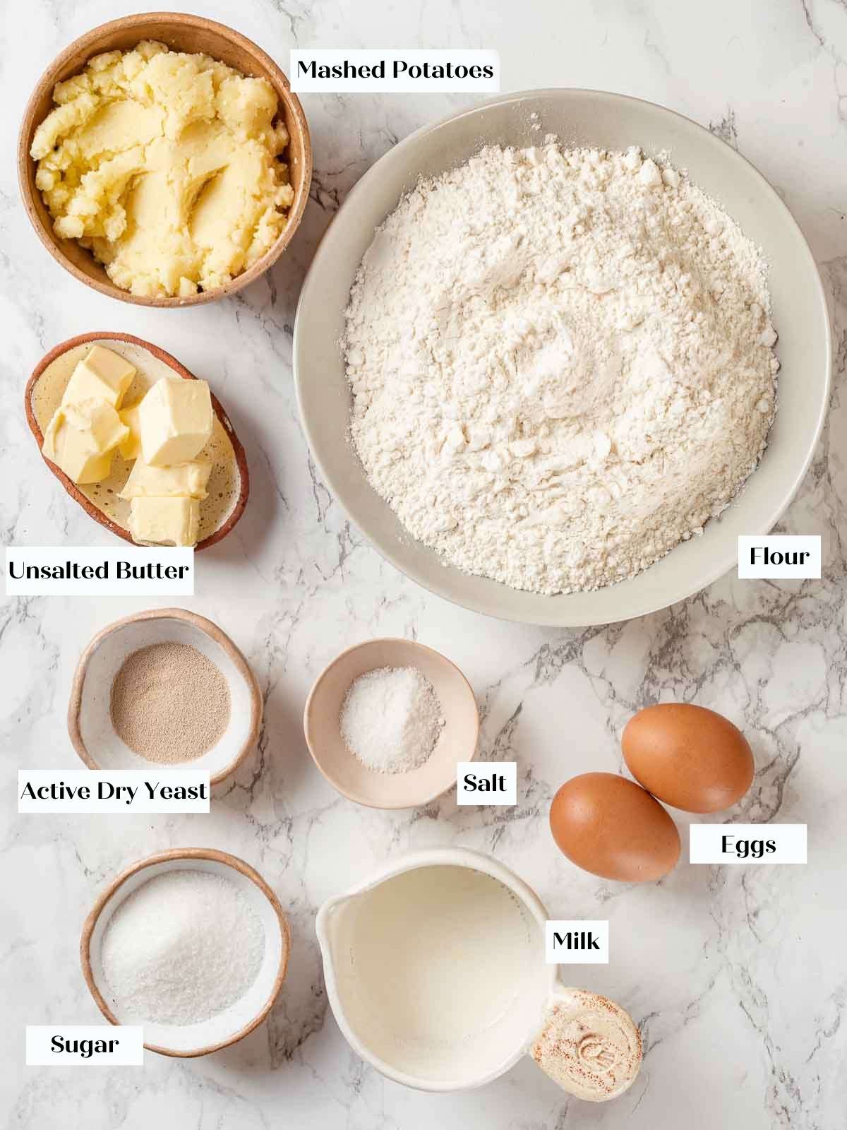 Ingredients for homemade potato bread neatly arranged on a white marble countertop.