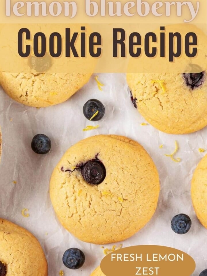 A batch of golden lemon blueberry cookies on parchment paper, with fresh blueberries around.