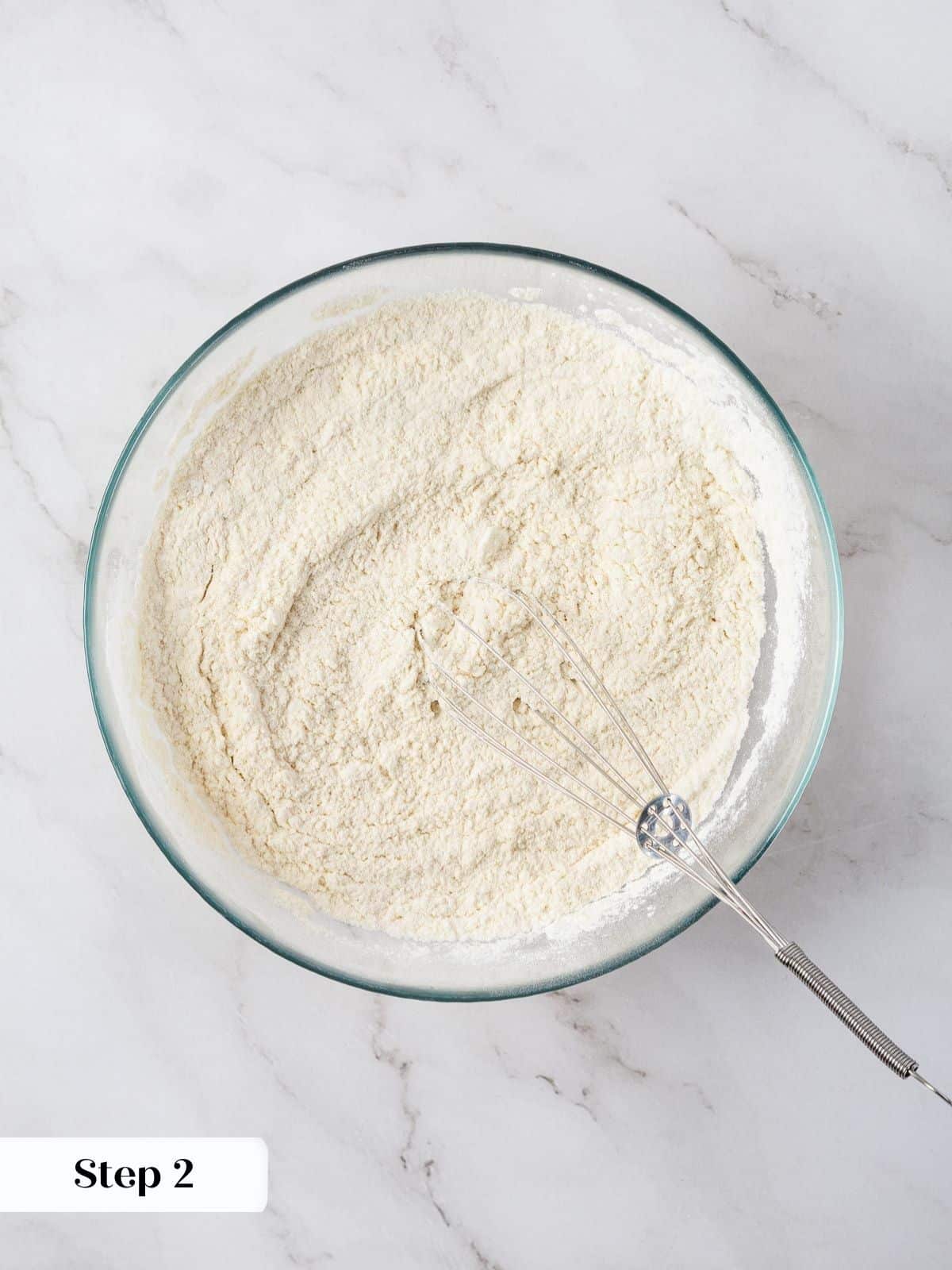 A glass bowl with flour, baking powder, and salt being whisked together.