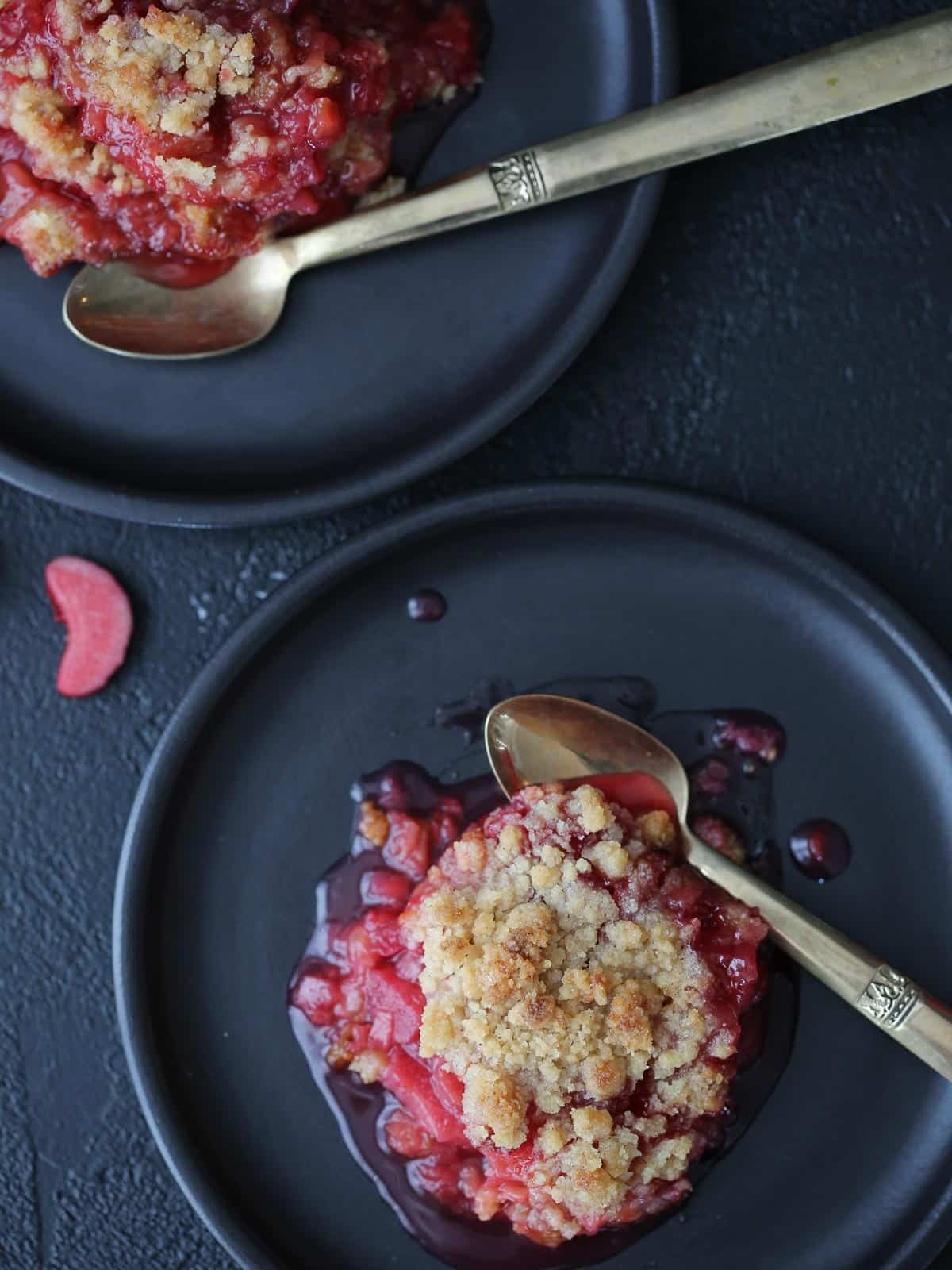 A silver spoon next to raspberry rhubarb crisp with thick fruit filling.