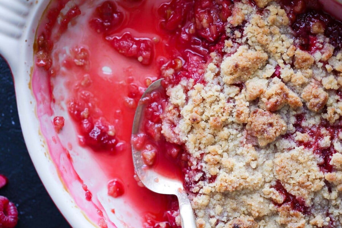 Raspberry rhubarb crisp baked in a white ceramic dish with a golden brown topping.