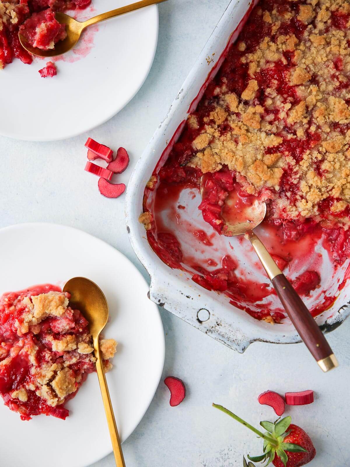 Fresh strawberries next to a baked dish of strawberry rhubarb crumble.