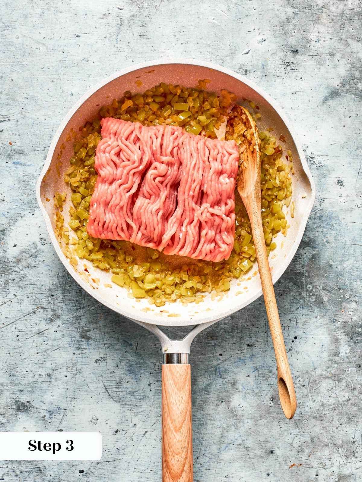 Ground turkey going into the pan to cook with onion and pepper.
