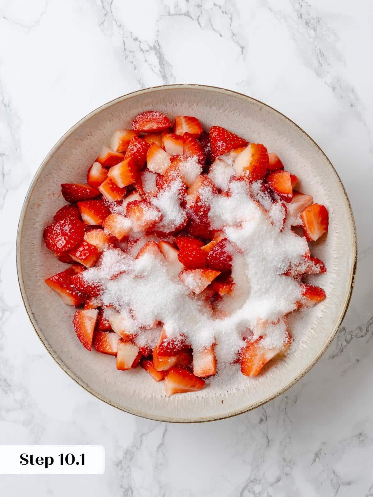 Freshly cut strawberries coated with sugar in a mixing bowl.