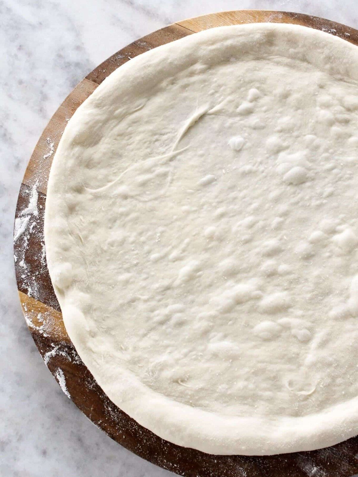 Unbaked pizza dough with raised edges and flour dusting.