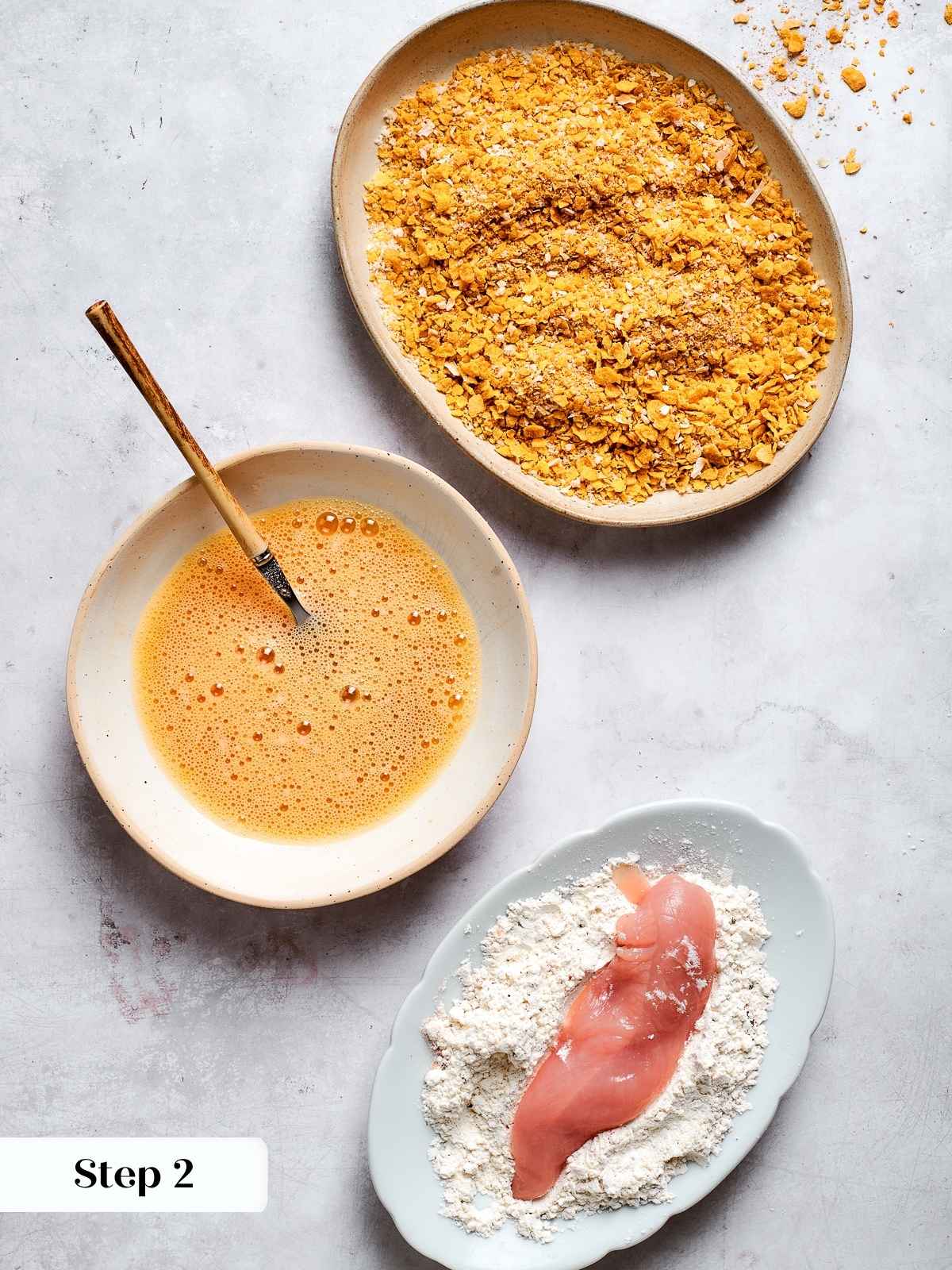 Chicken tenders being coated in seasoned flour mixture on a plate during prep process.
