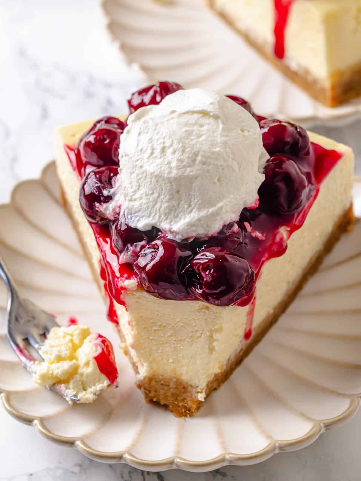 A slice of cheesecake with one bite taken, showing layers of crust, cream, and topping.