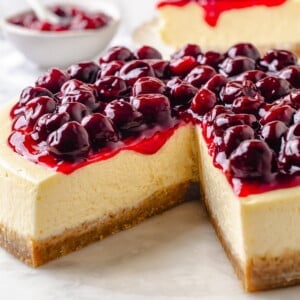 Homemade cherry topping drips down the side of creamy cheesecake with a golden brown crust.