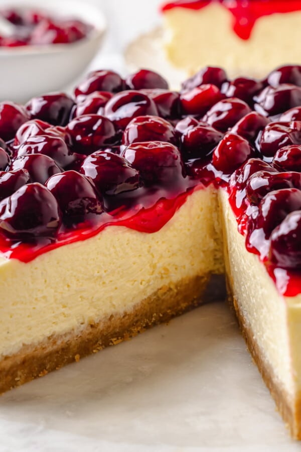 Homemade cherry topping drips down the side of creamy cheesecake with a golden brown crust.