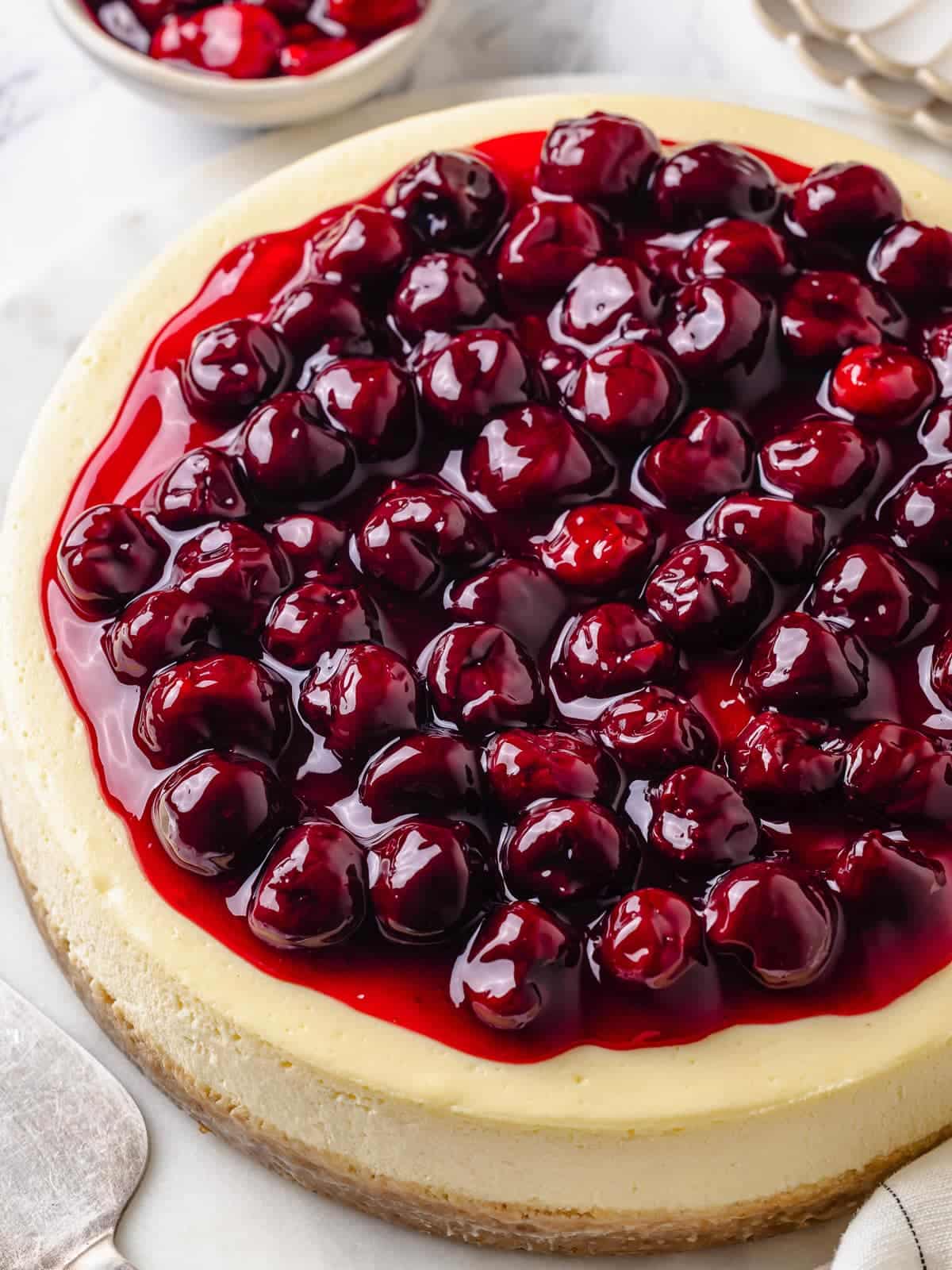 A whole cherry cheesecake with smooth filling and cherry topping on a white cake stand.