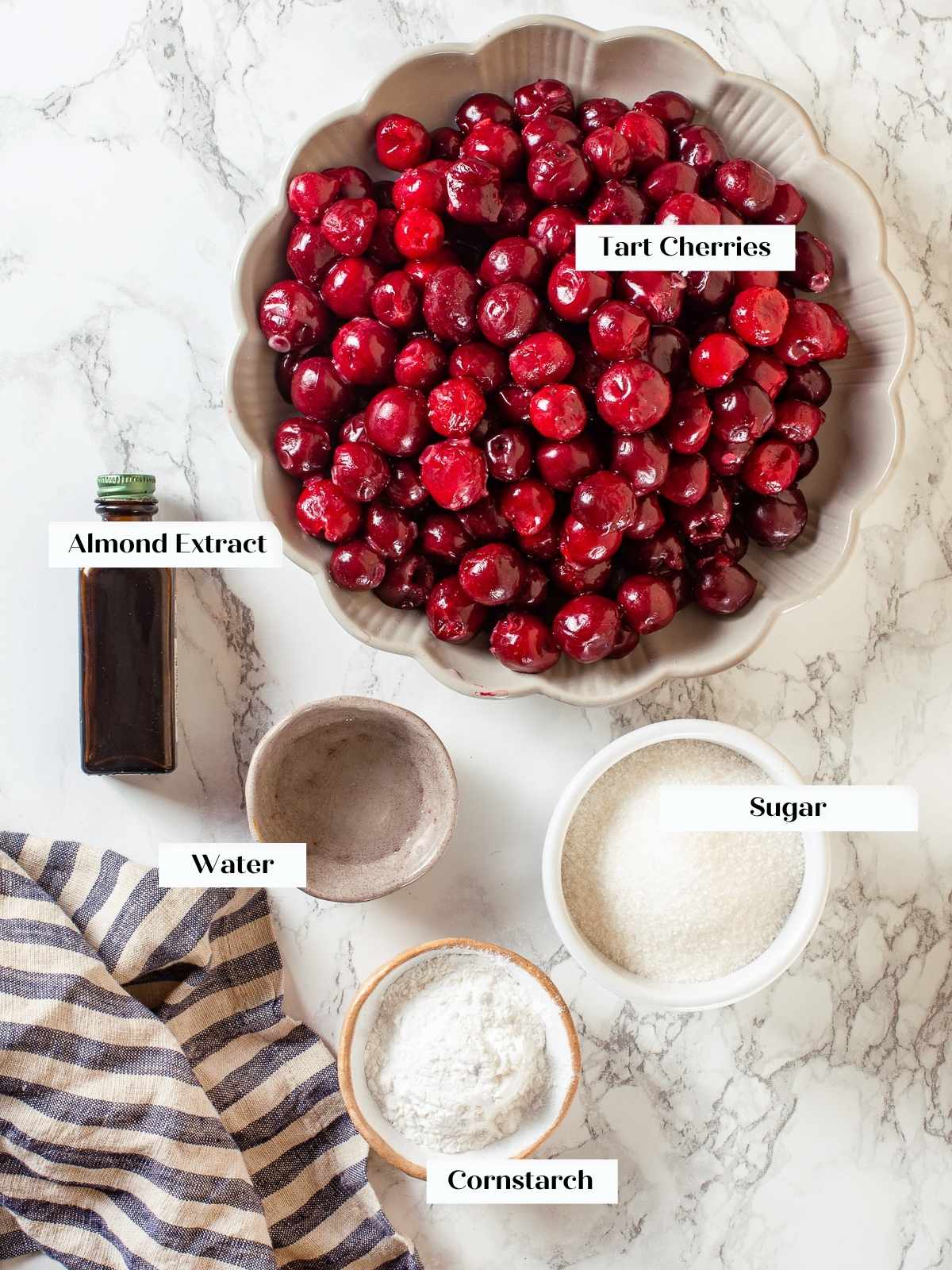 Ingredients for cherry pie filling laid out on counter, including cherries, sugar, and almond extract.