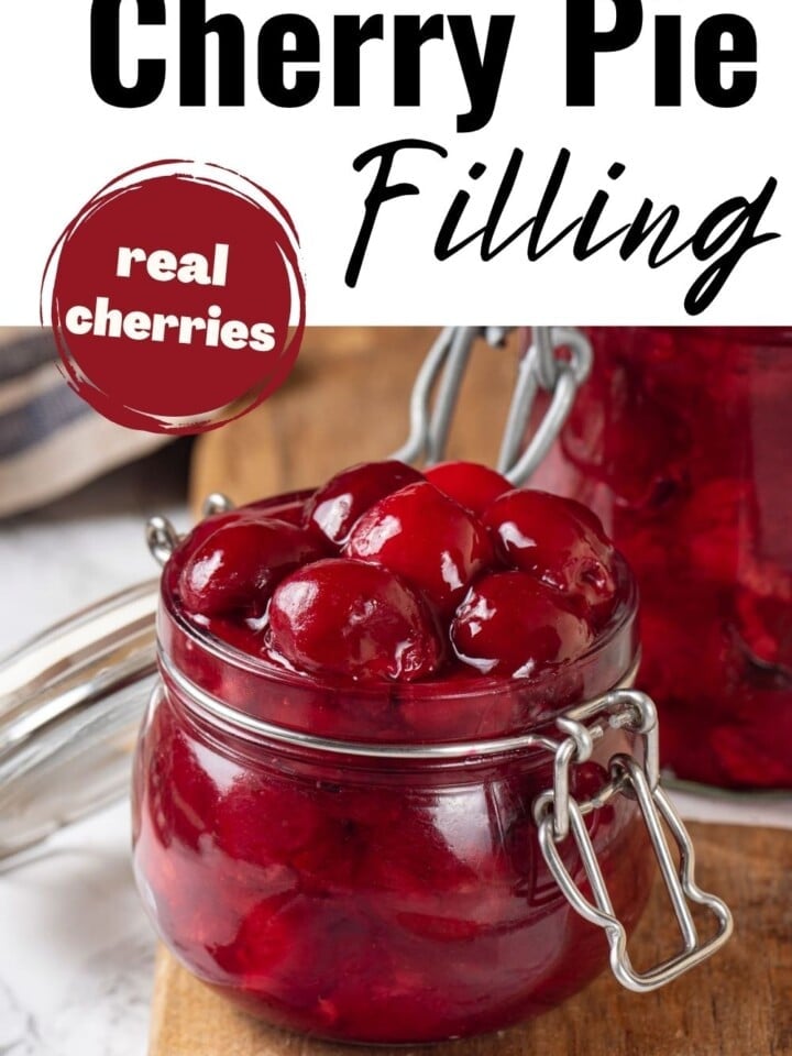 Mason jars filled with finished cherry pie filling, lined up on a wooden board.