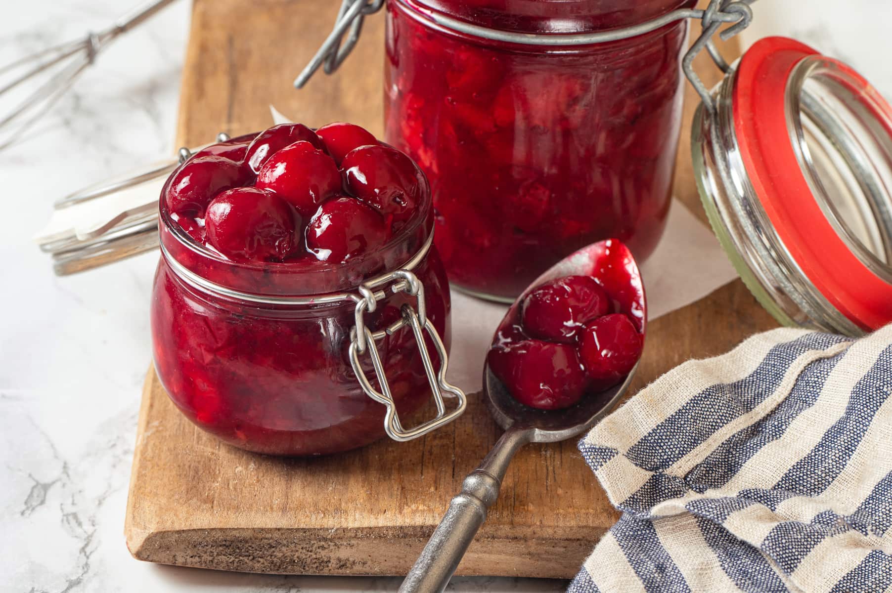 Thick, glossy cherry pie filling clings to spoon, showing texture and visible chunks of fruit.