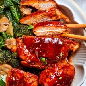 Thick gochujang sauce coating pan-seared chicken pieces with mushrooms in a bowl.