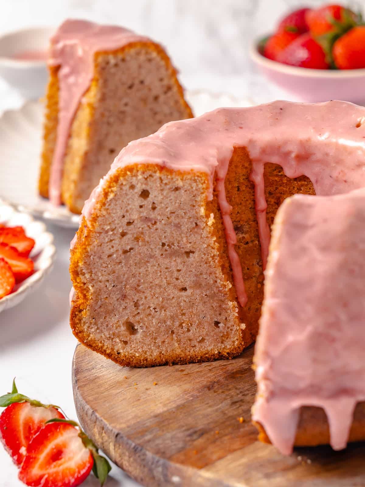 Sliced pound cake arranged on a cutting board, surrounded by strawberries and crumbs.