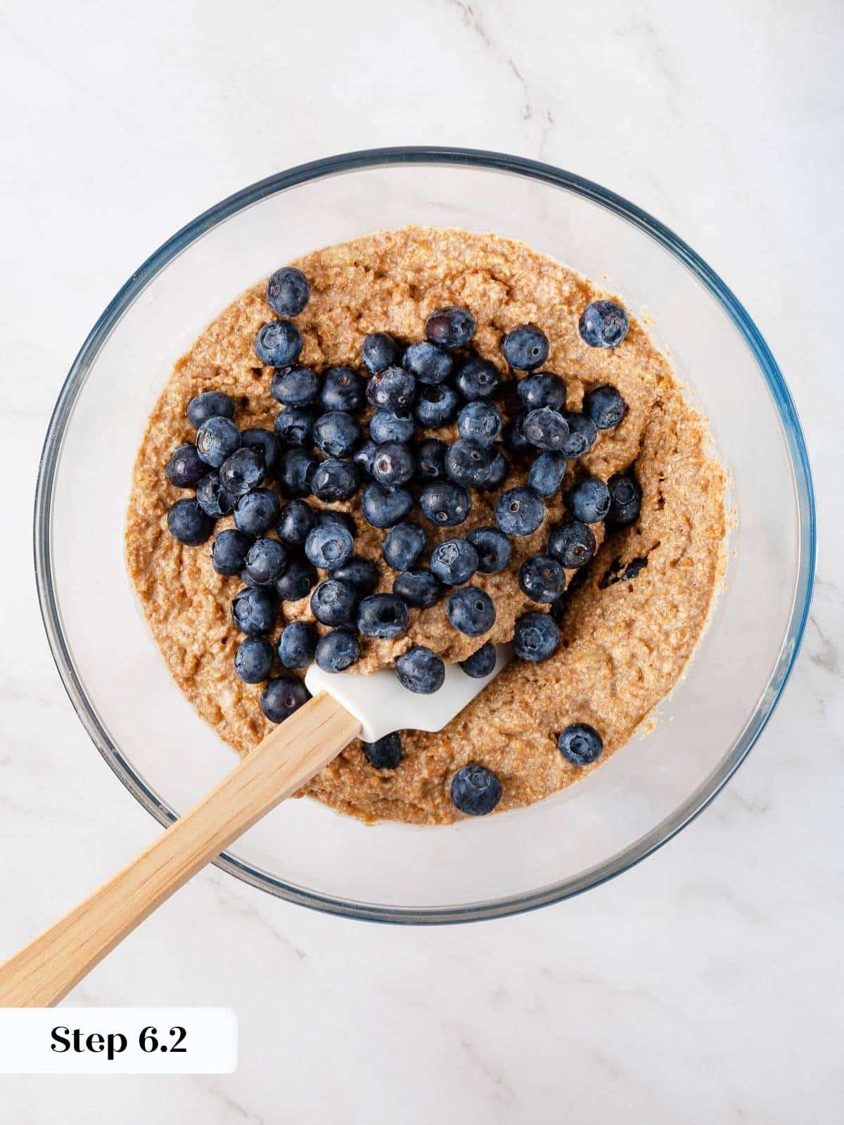 Blueberries gently folded into banana muffin batter with a spatula to avoid overmixing.