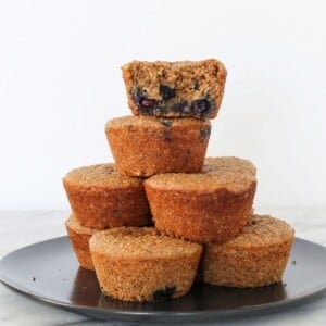A banana protein muffin with one bite taken, stacked with others to show soft inside texture.