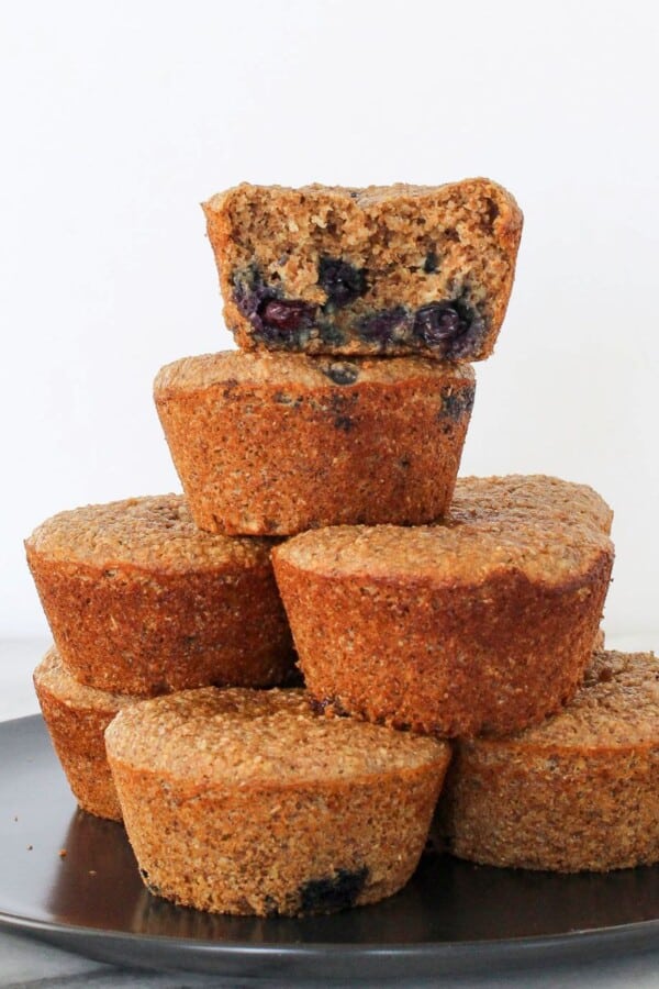 A banana protein muffin with one bite taken, stacked with others to show soft inside texture.
