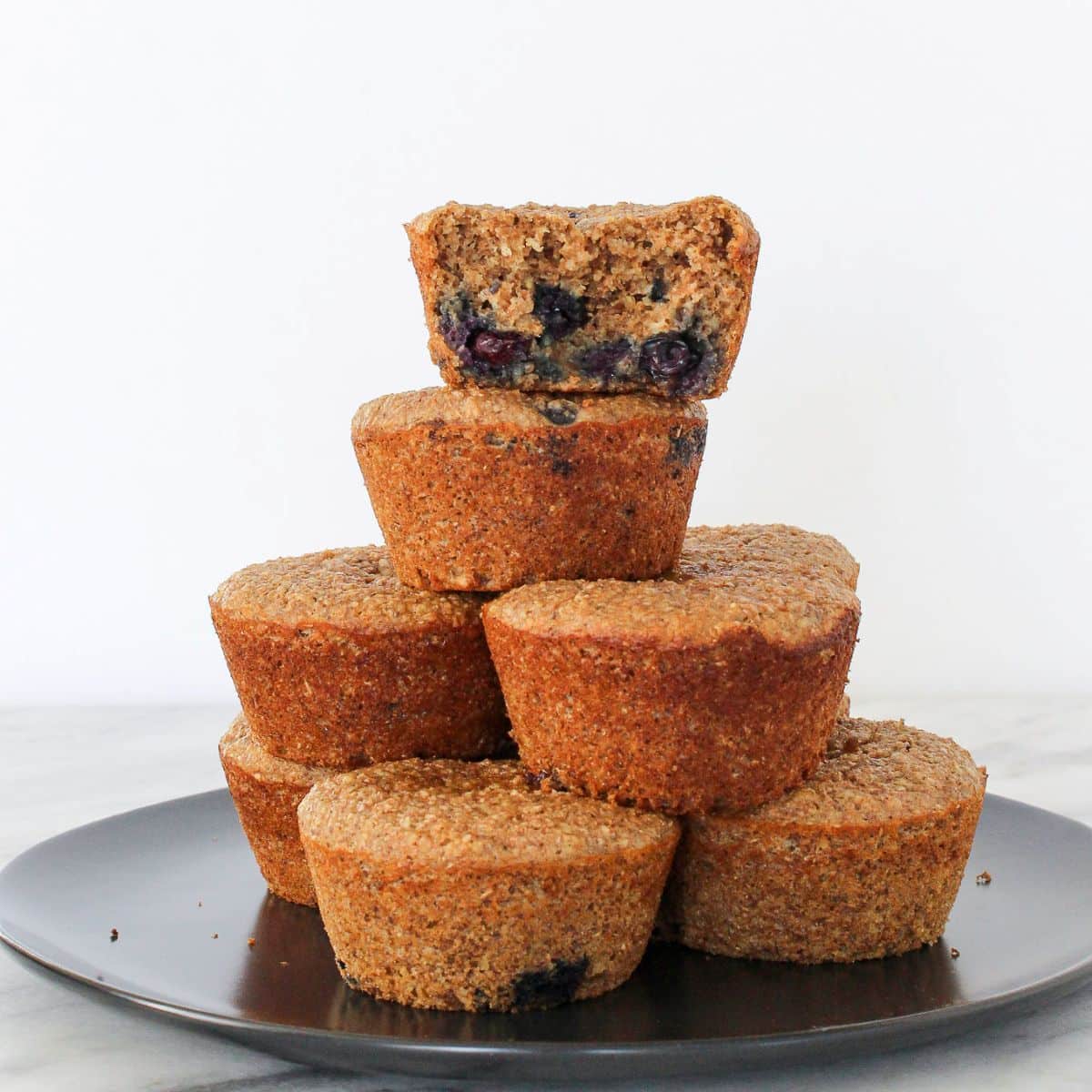 A banana protein muffin with one bite taken, stacked with others to show soft inside texture.