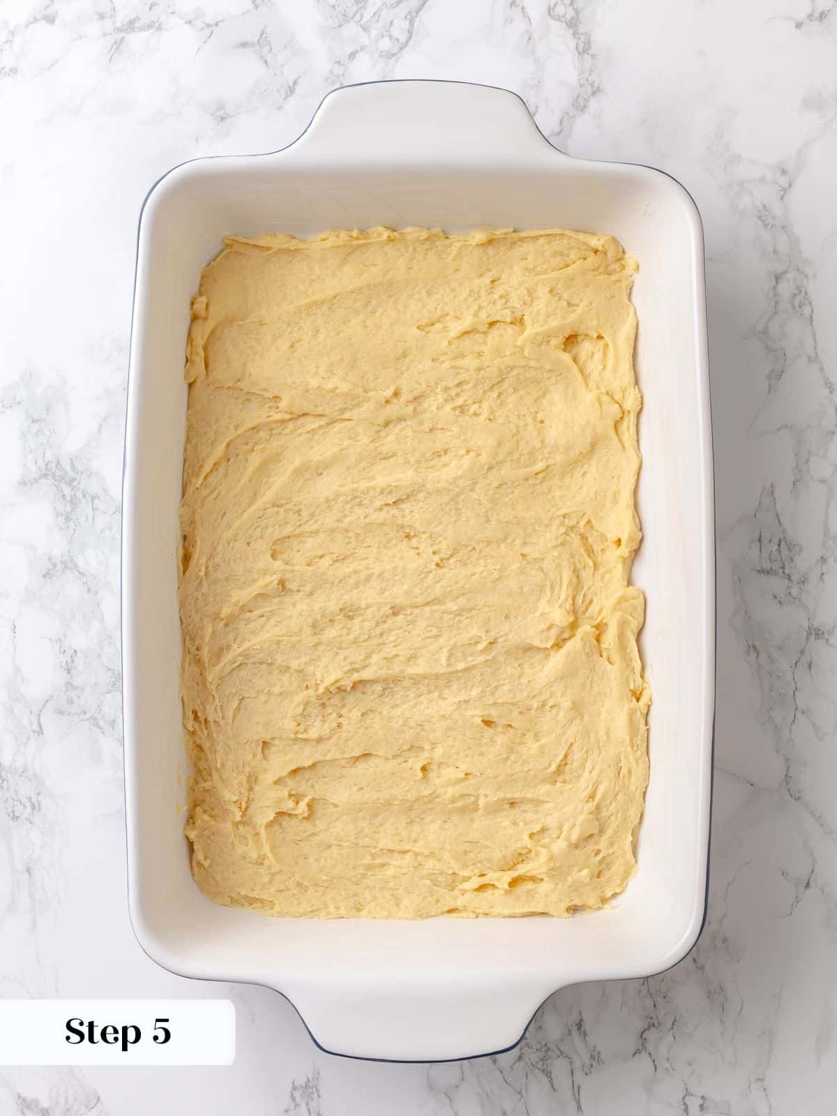 Cake dough is pressed into the dish with a spatula to create an even base.