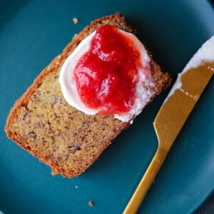 Moist banana bread slice shown with thick jam spread, resting on a small plate.
