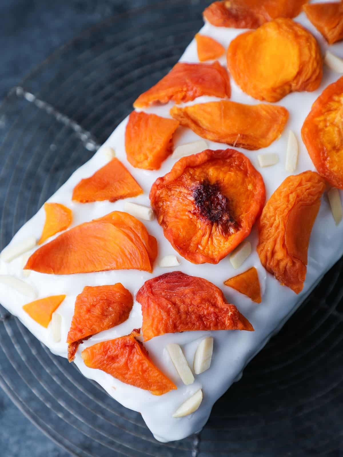 Glazed peach cake topped with dried peaches and almonds on a cooling rack.