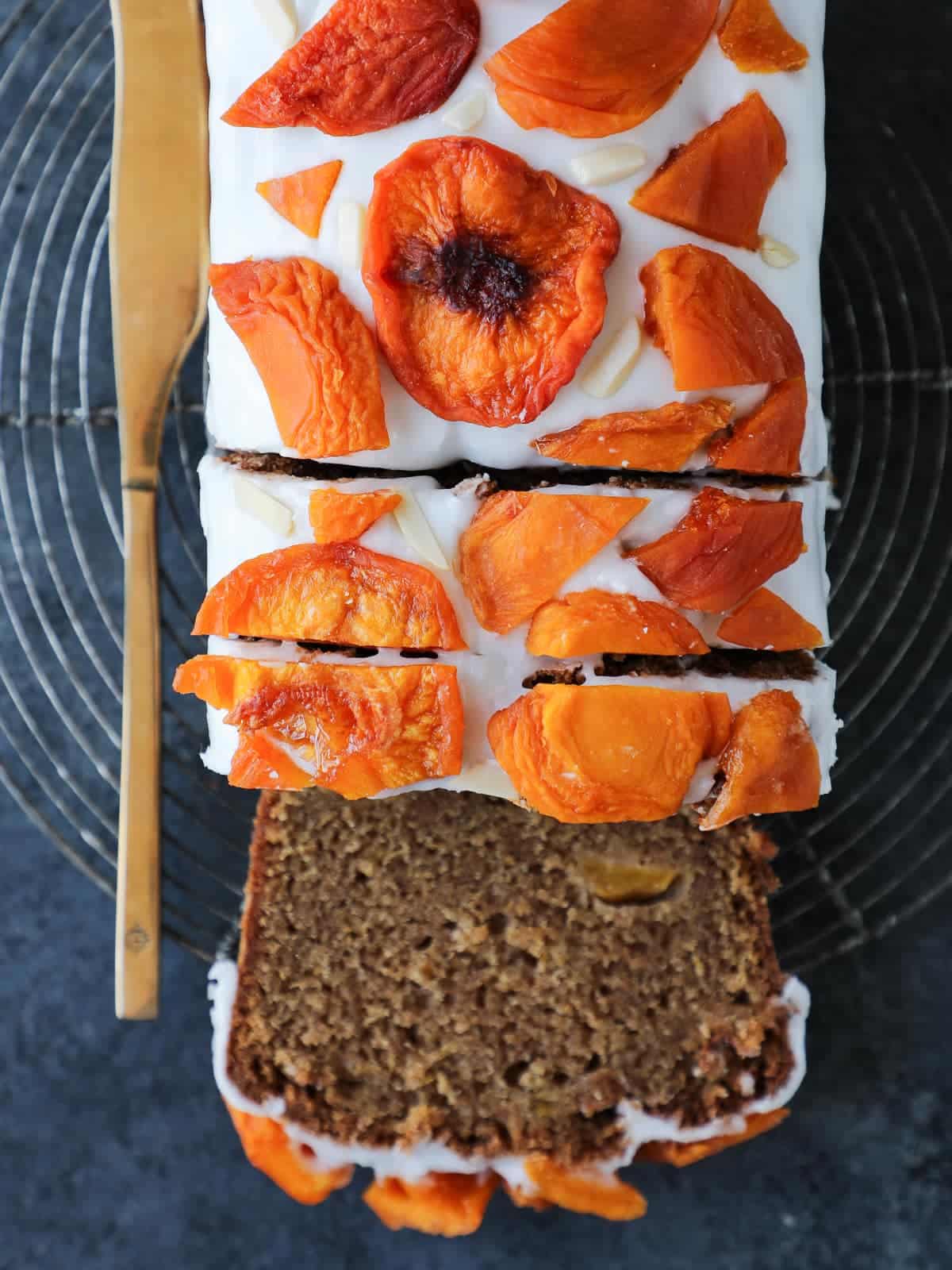 Partially sliced loaf of peach cake revealing tender interior and fruit throughout.