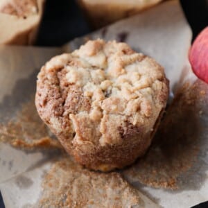 Fresh muffin made with peaches, resting on parchment with golden top and crisp edges.