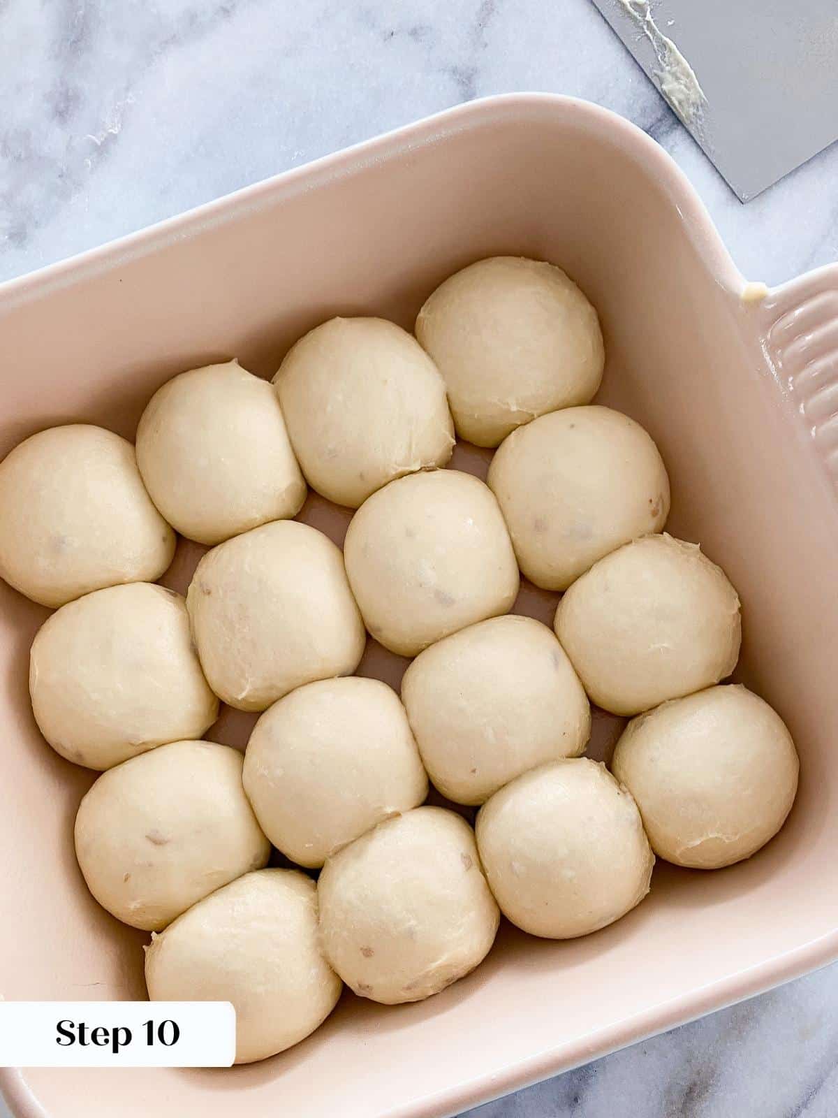 Unproofed potato dough rolls arranged in a baking dish before rising.