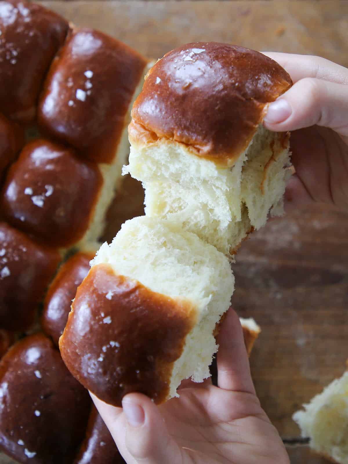 "Breaking a warm, fluffy potato roll by hand to reveal its tender interior.