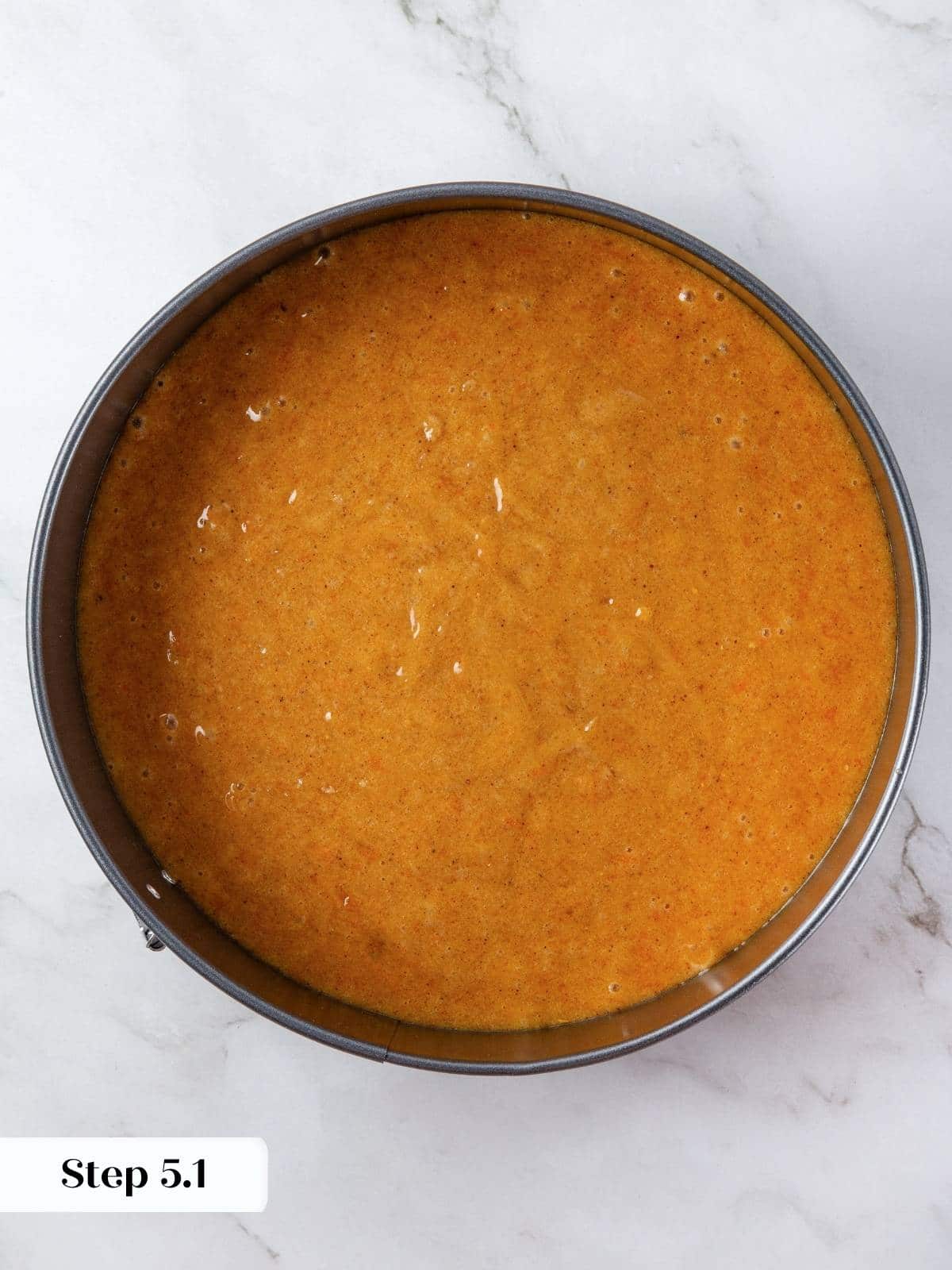 A filled cake pan with golden orange pumpkin batter smoothed across the top with a spatula.