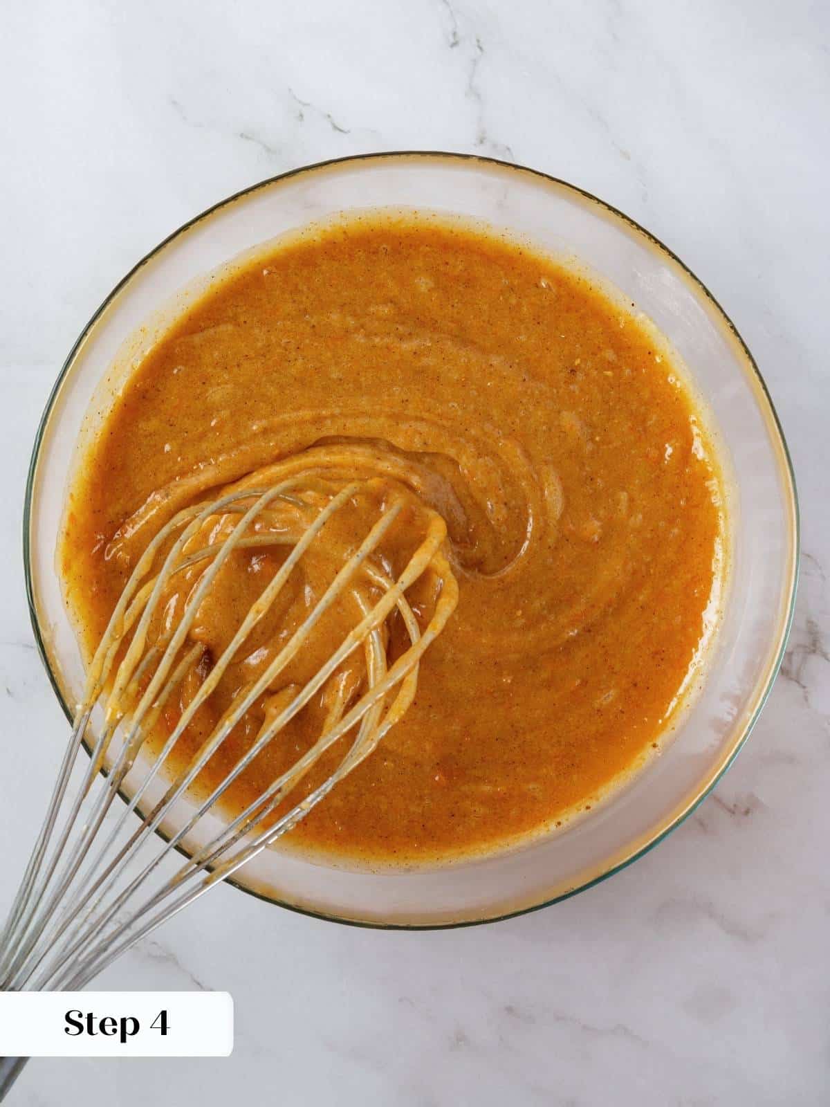 Spiced pumpkin batter swirled in a large mixing bowl, glossy and orange before baking.