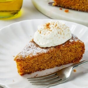 A fork next to soft pumpkin cake on a dessert plate, crumb falling onto the table.