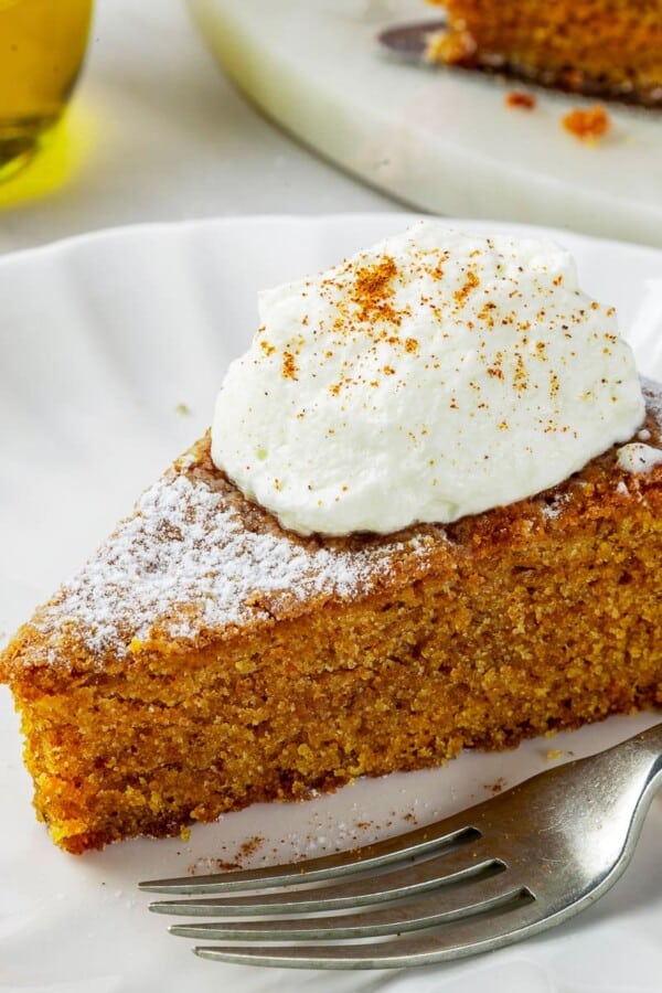 A fork next to soft pumpkin cake on a dessert plate, crumb falling onto the table.