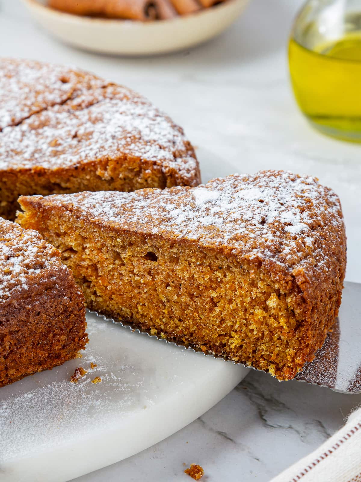 Full pumpkin cake sits centered on a white ceramic stand, sliced and ready for sharing.
