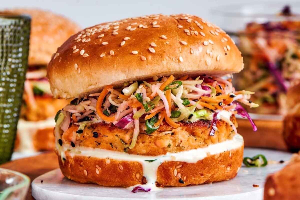 Fully assembled salmon burgers with slaw and sauce lined up and ready to eat.