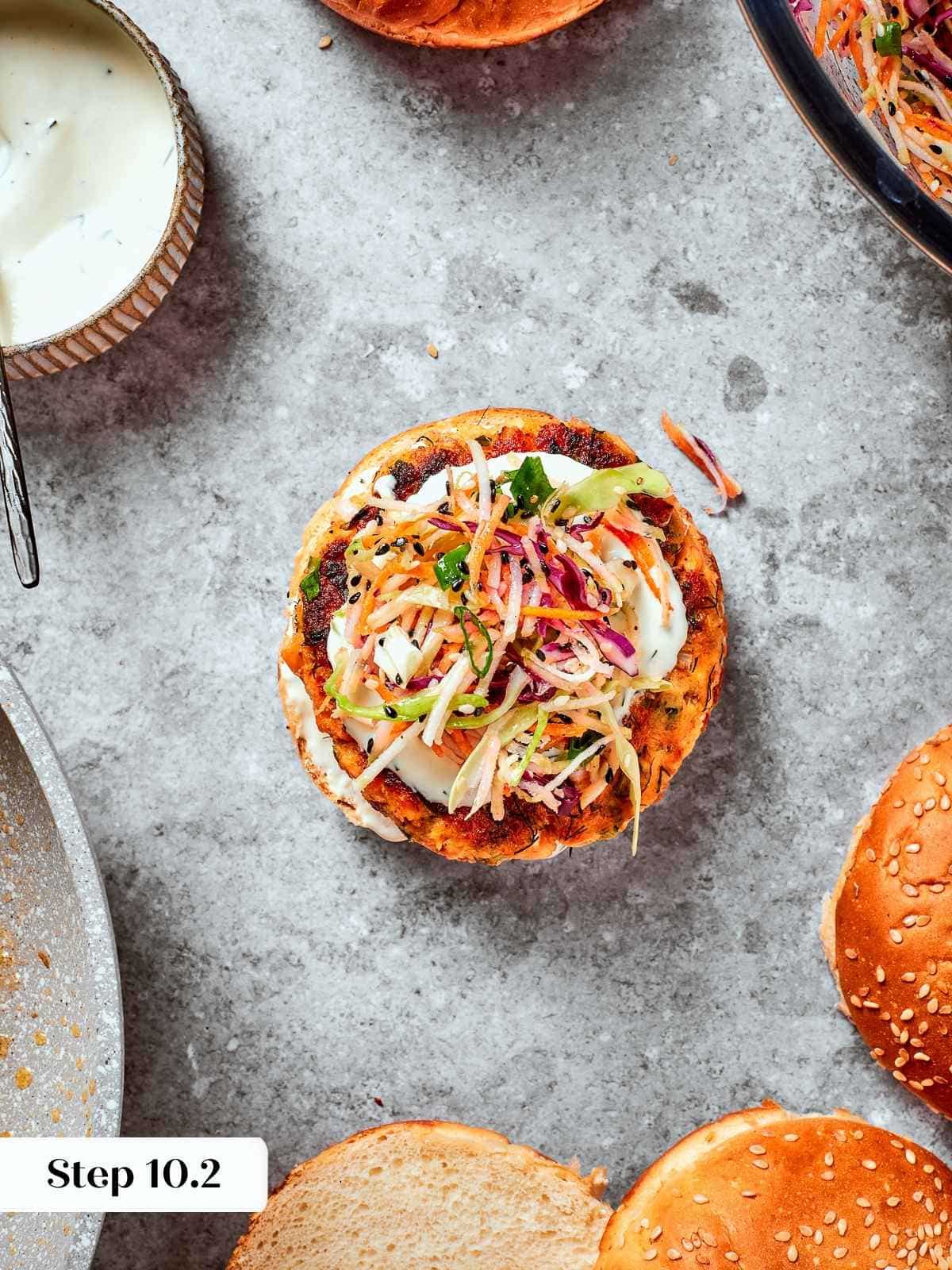 Assembled burger with top bun off showing layers of salmon, slaw, and sauce.