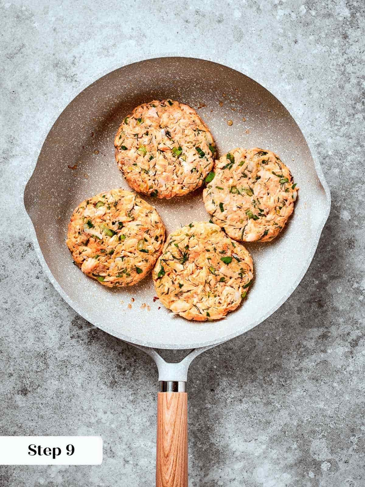 Salmon burger patties sizzling in a pan, developing golden brown crust.