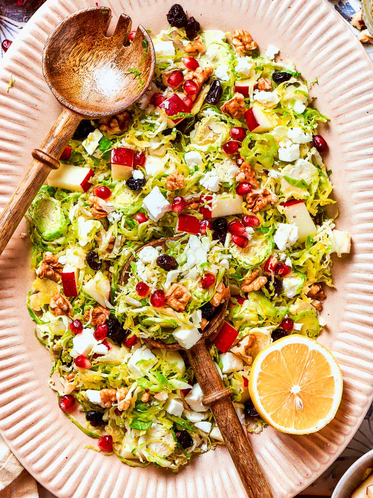 A fresh lemon sliced in half next to a bowl of shredded Brussels sprouts salad.
