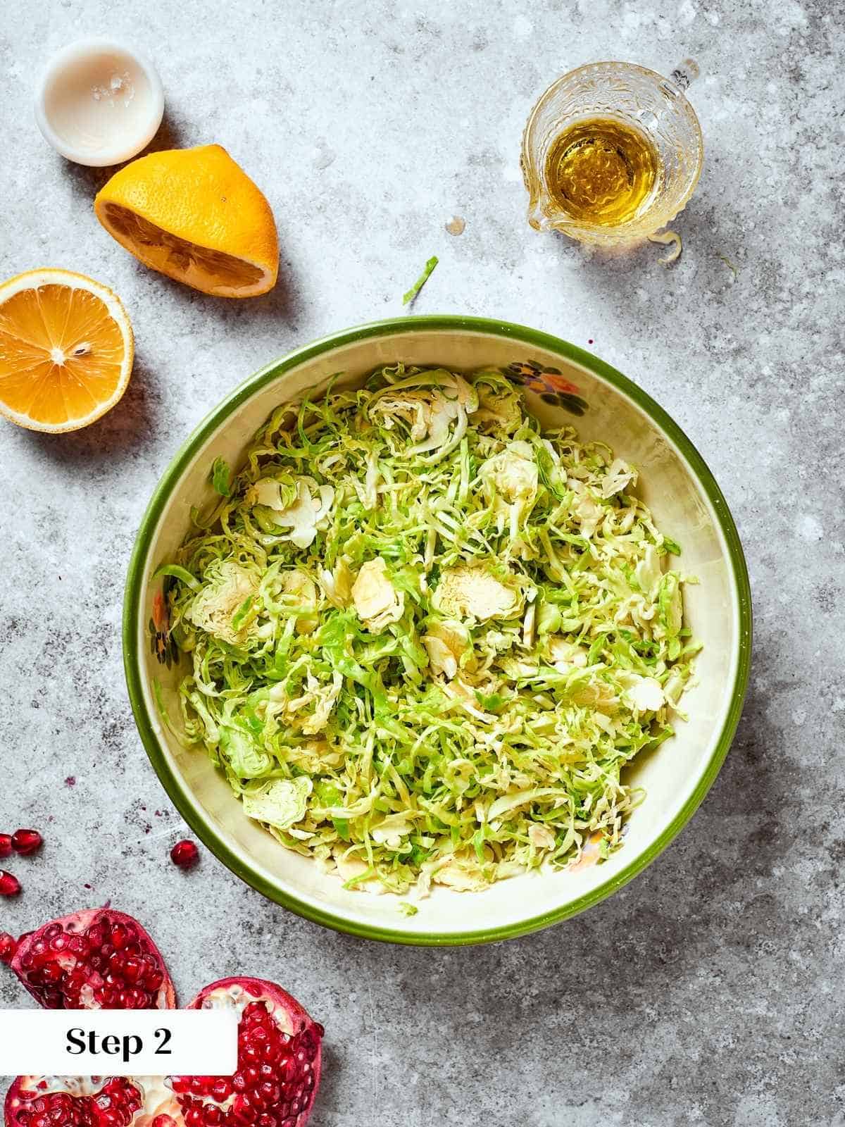 Lemon juice and olive oil poured over shredded Brussels sprouts in a mixing bowl.