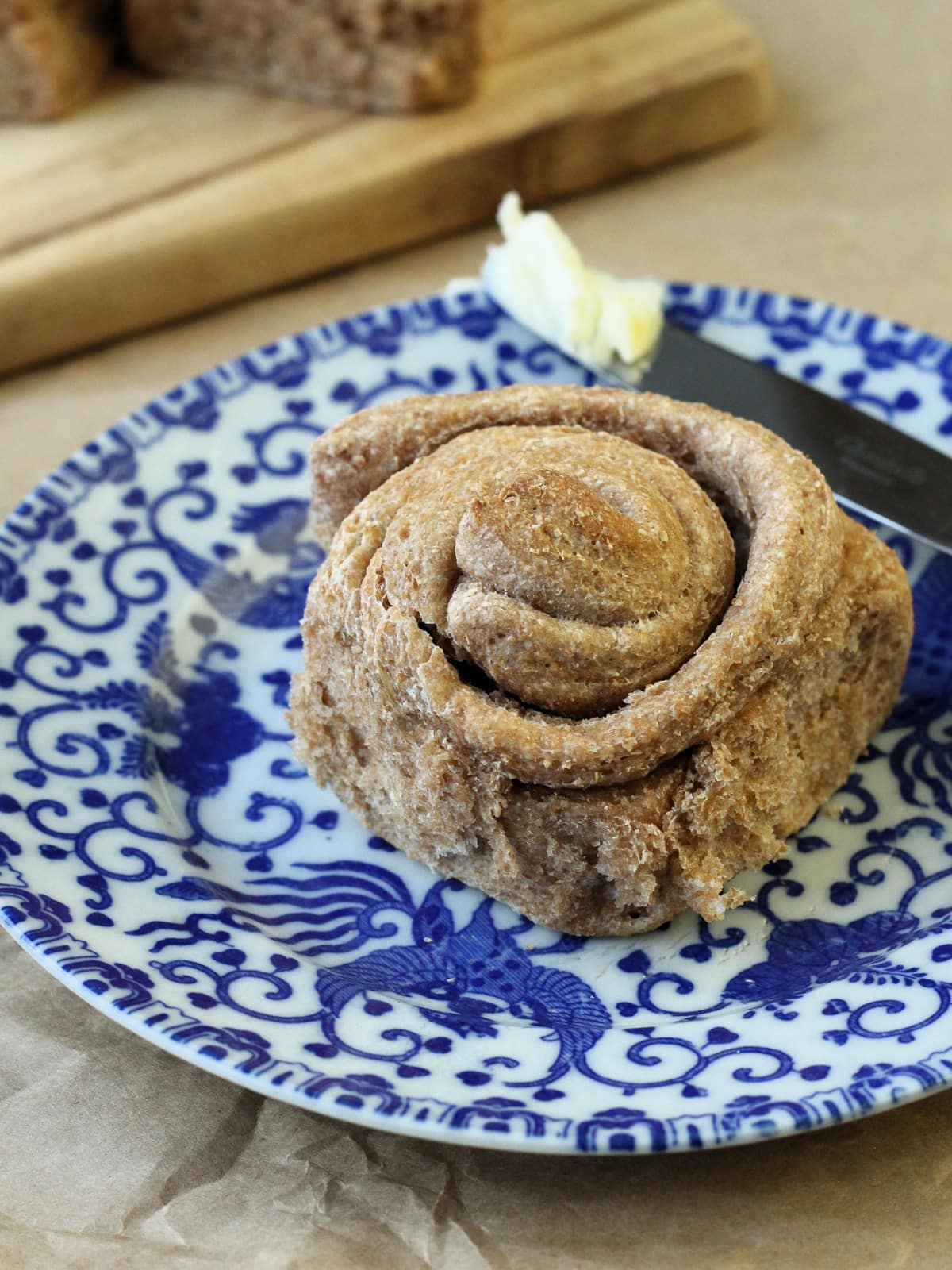 A buttered knife rests beside a warm roll, melted butter glistening over the golden crust.