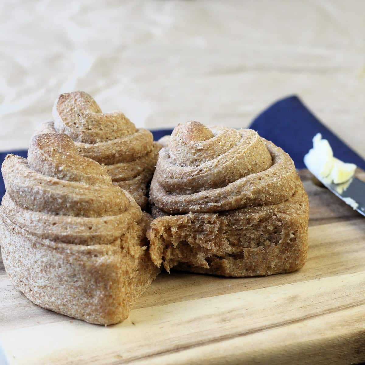 Several whole wheat rolls rest on a wooden board, showcasing their rustic homemade finish.