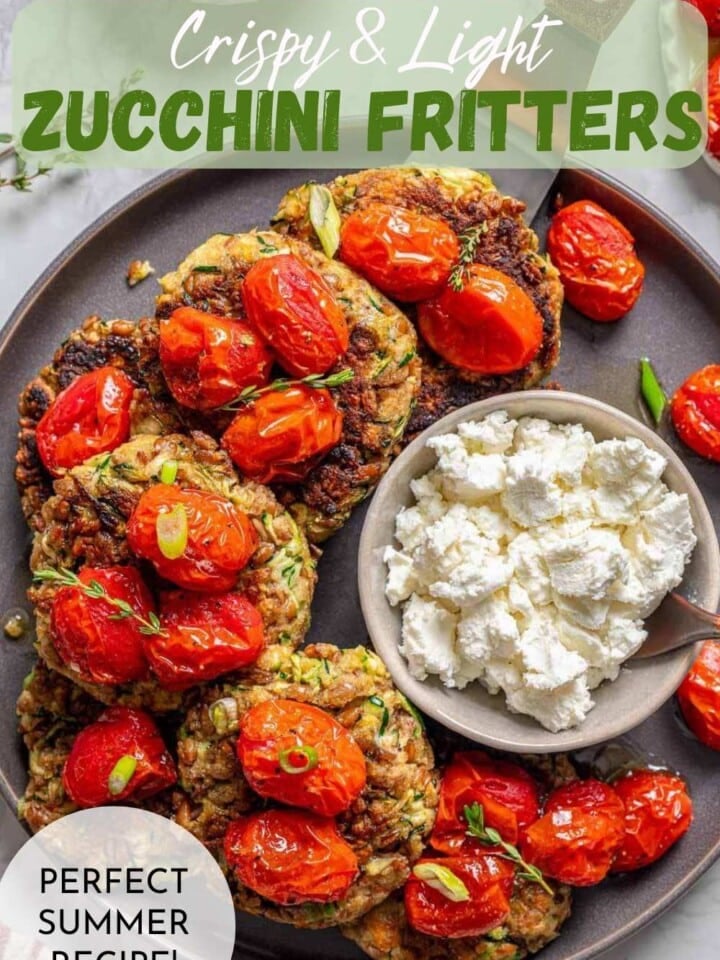 A round plate displaying golden brown zuchhini fritters with roasted tomatoes and a small bowl of goat cheese for topping.