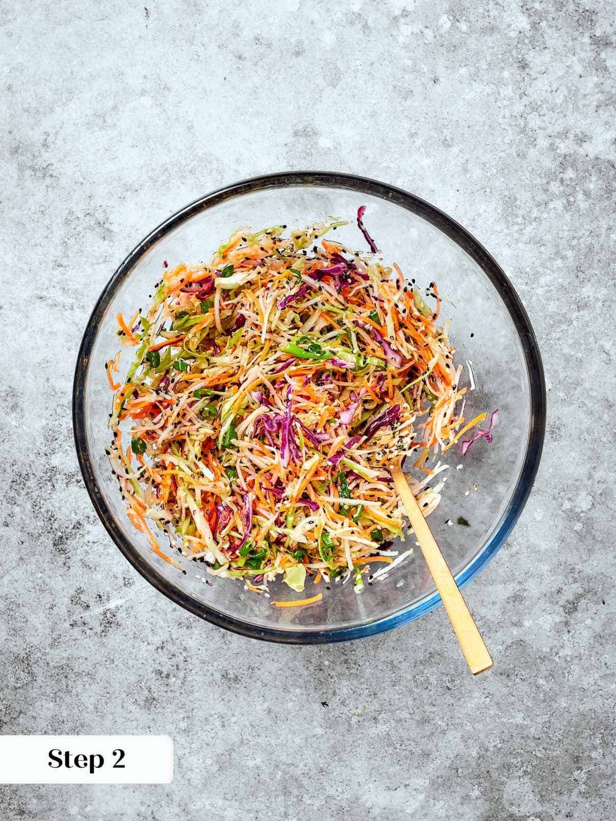 Broccoli slaw fully combined with dressing in a bowl, sesame seeds and carrots evenly coated.