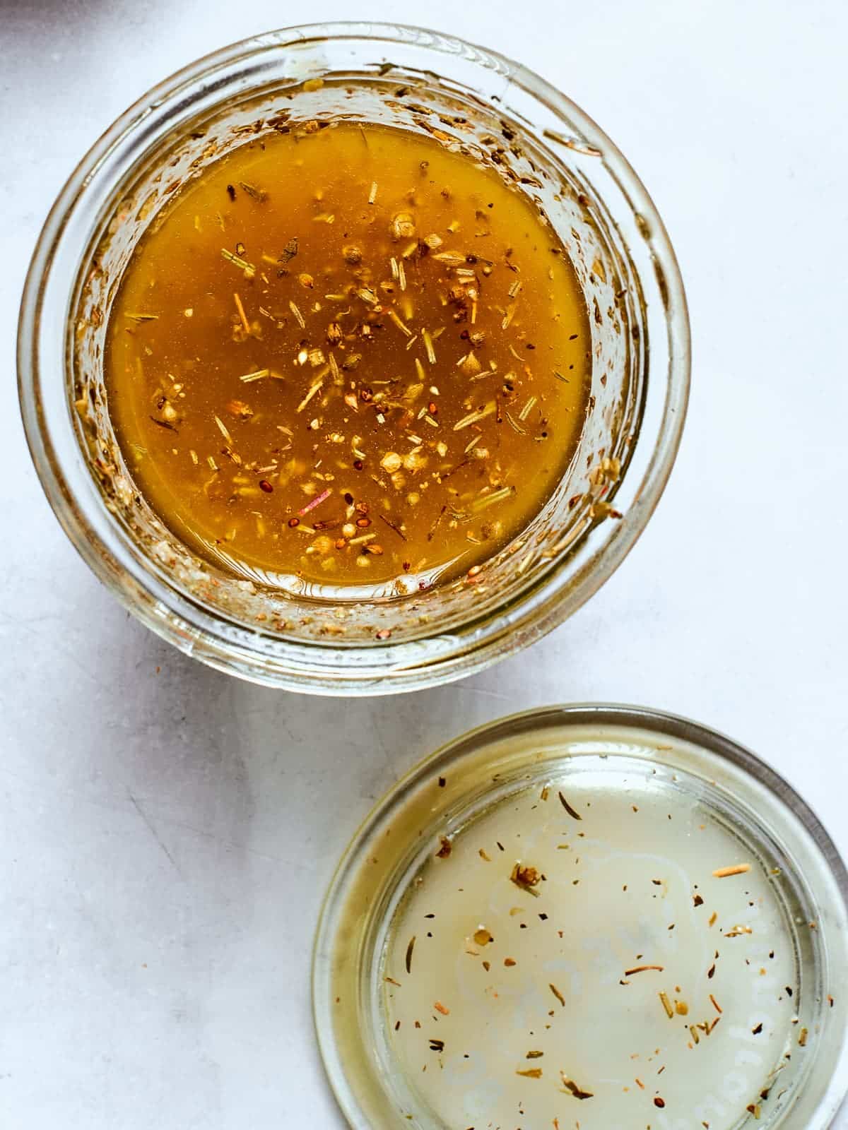 Clear glass jar filled with Italian salad dressing and visible herbs.