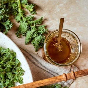 Jar of Italian salad dressing set beside fresh kale leaves on a counter.
