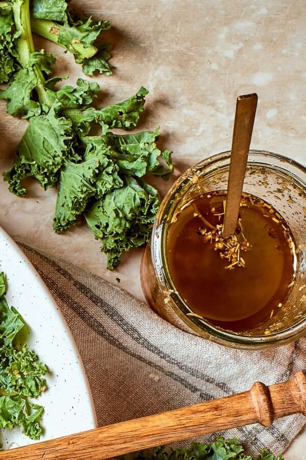 Jar of Italian salad dressing set beside fresh kale leaves on a counter.