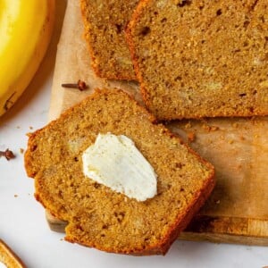 Slice of pumpkin banana bread spread with melting butter on warm crumb.
